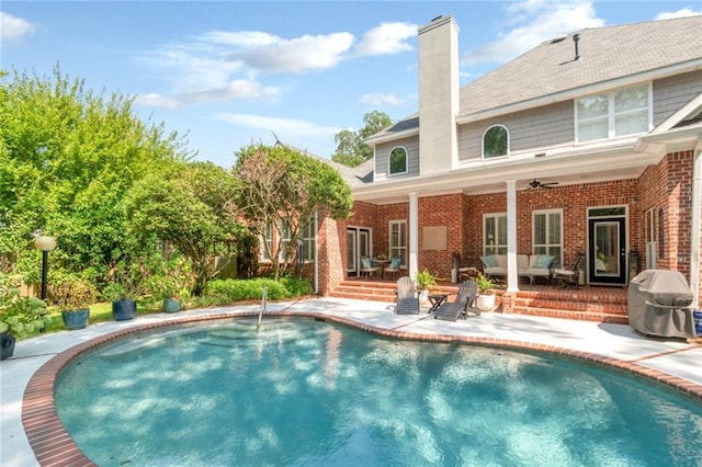 rear view of property featuring a patio, an outdoor pool, a chimney, ceiling fan, and brick siding