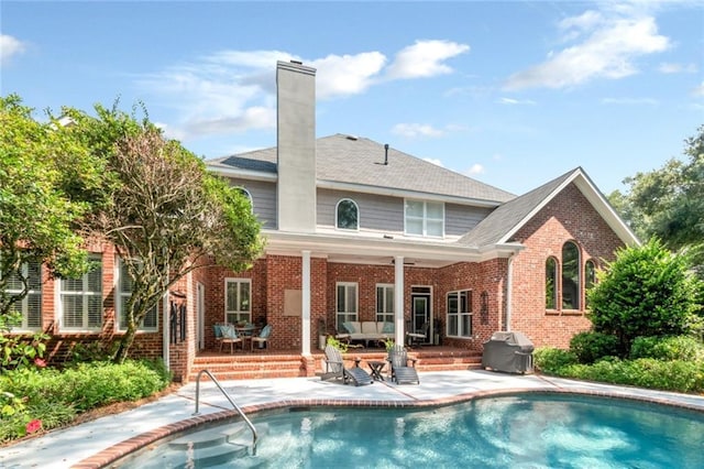 rear view of property featuring a patio, an outdoor pool, brick siding, and a chimney