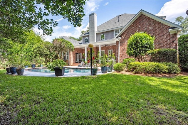 rear view of property with brick siding, a lawn, a chimney, a patio area, and an outdoor pool