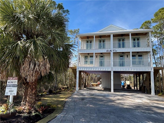 coastal home featuring a balcony, metal roof, aphalt driveway, and a carport