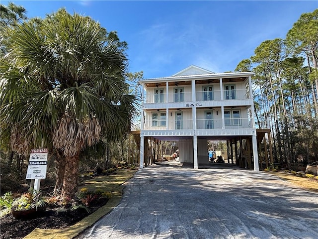 raised beach house featuring aphalt driveway, a balcony, covered porch, a ceiling fan, and a carport