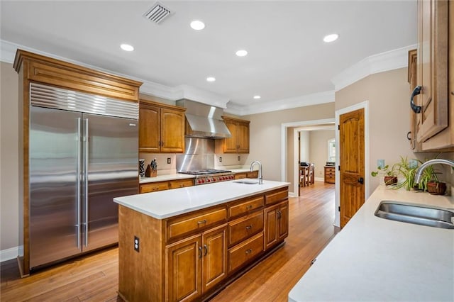 kitchen featuring wall chimney exhaust hood, an island with sink, appliances with stainless steel finishes, and sink