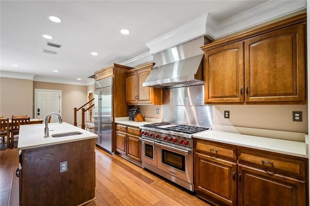 kitchen with crown molding, wall chimney exhaust hood, sink, a kitchen island with sink, and high end appliances