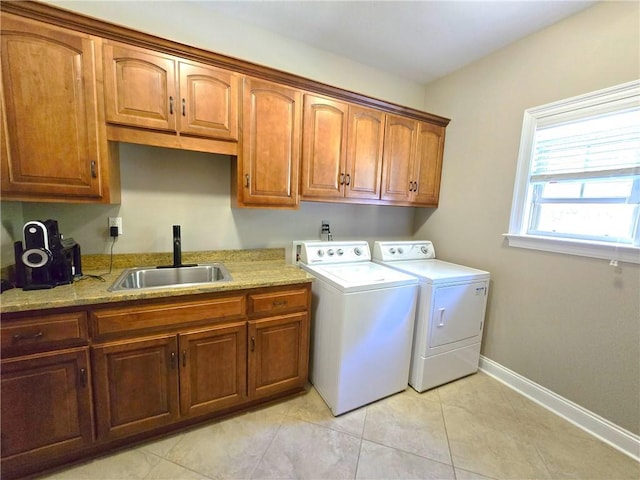 clothes washing area with sink, washing machine and dryer, light tile patterned floors, and cabinets