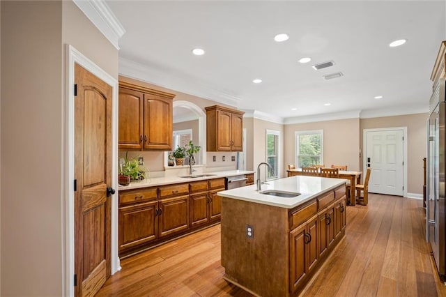 kitchen with sink, light wood-type flooring, a kitchen island with sink, and crown molding