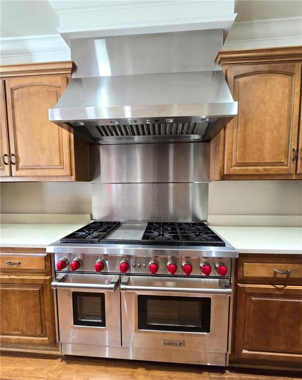 kitchen featuring double oven range, wall chimney range hood, and crown molding