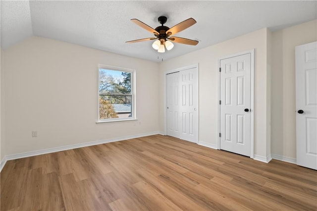 unfurnished bedroom with ceiling fan, vaulted ceiling, light hardwood / wood-style flooring, multiple closets, and a textured ceiling