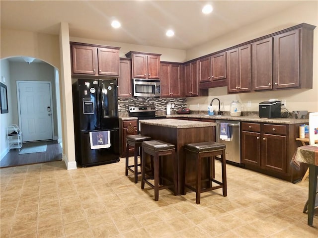 kitchen featuring a kitchen island, dark brown cabinets, appliances with stainless steel finishes, a kitchen bar, and sink