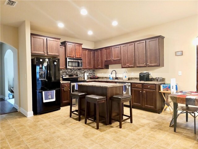 kitchen with a sink, a kitchen island, a kitchen breakfast bar, stainless steel appliances, and arched walkways