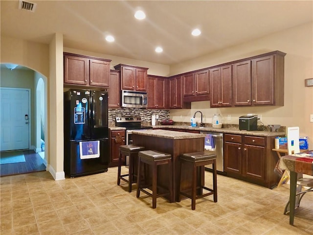 kitchen featuring a kitchen breakfast bar, light stone countertops, a center island, stainless steel appliances, and sink