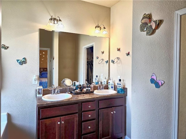 full bathroom with a spacious closet, double vanity, a sink, and ensuite bath