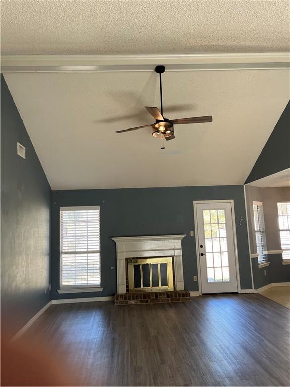 unfurnished living room featuring vaulted ceiling, a brick fireplace, dark wood-type flooring, and a textured ceiling