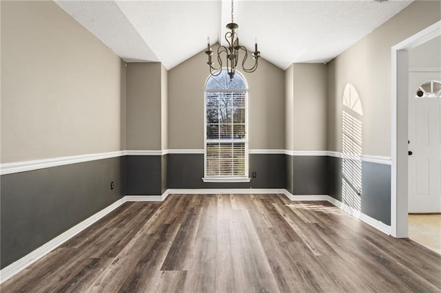 unfurnished dining area with baseboards, wood finished floors, vaulted ceiling, a textured ceiling, and a notable chandelier