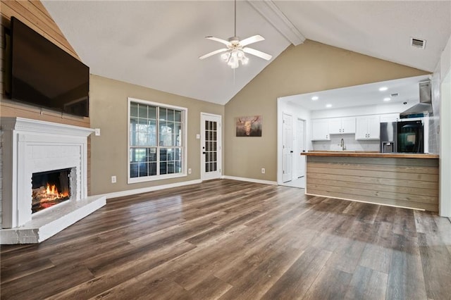 unfurnished living room featuring dark wood-style floors, beam ceiling, a fireplace, visible vents, and baseboards