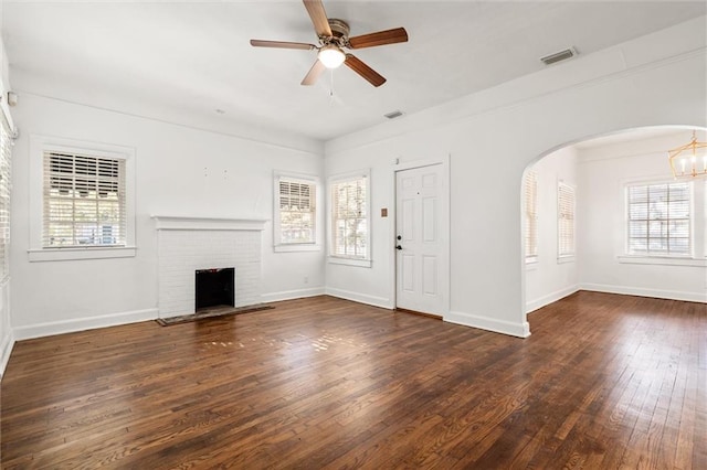 unfurnished living room with a fireplace, dark hardwood / wood-style flooring, ceiling fan with notable chandelier, and a wealth of natural light