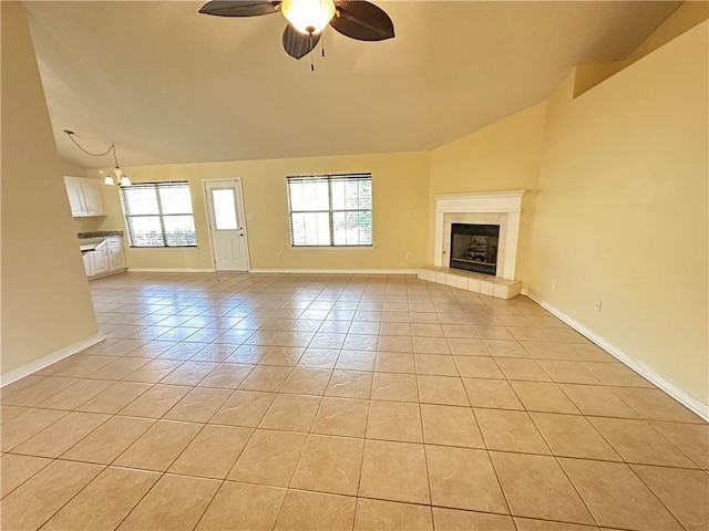 unfurnished living room with ceiling fan, vaulted ceiling, a tile fireplace, and light tile patterned floors