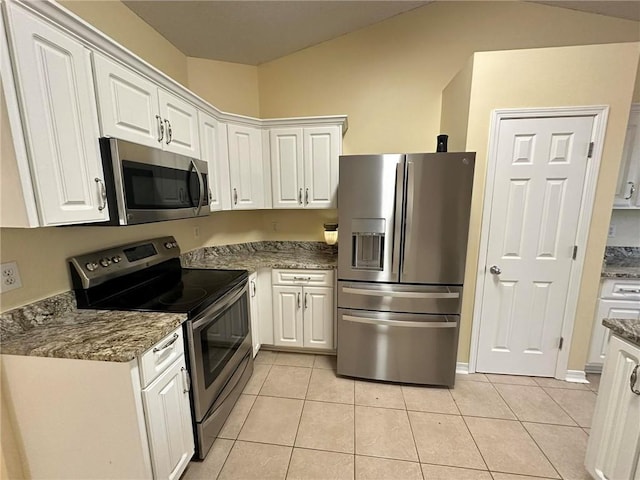 kitchen with appliances with stainless steel finishes, light tile patterned floors, dark stone counters, and white cabinets