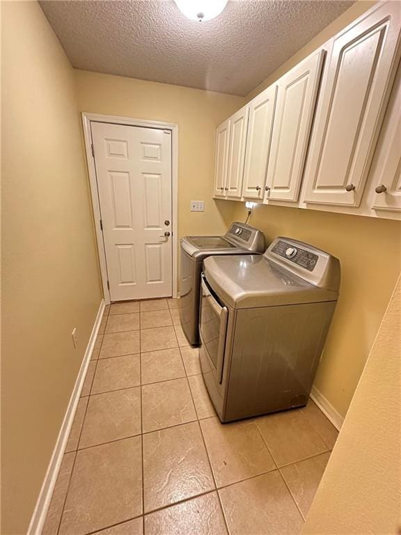 laundry room with cabinets, light tile patterned floors, a textured ceiling, and washer and clothes dryer