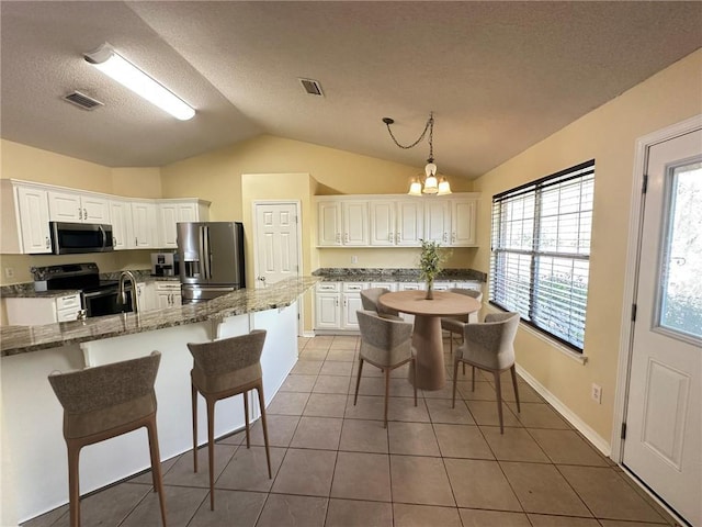 kitchen with white cabinetry, decorative light fixtures, dark stone countertops, appliances with stainless steel finishes, and dark tile patterned floors