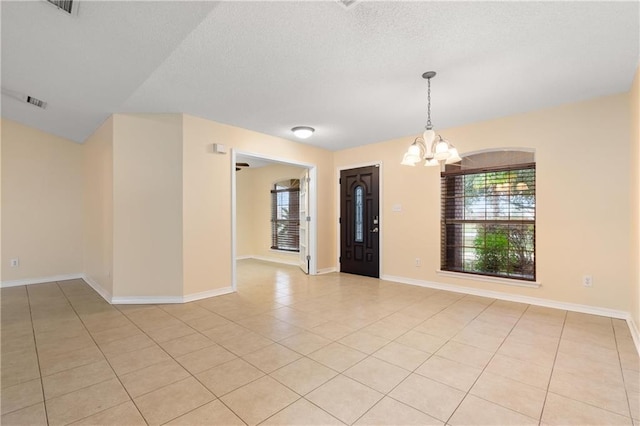 tiled empty room with a chandelier and a textured ceiling