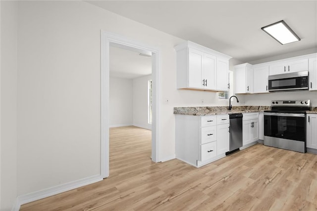 kitchen featuring light wood finished floors, stainless steel appliances, white cabinets, a sink, and light stone countertops