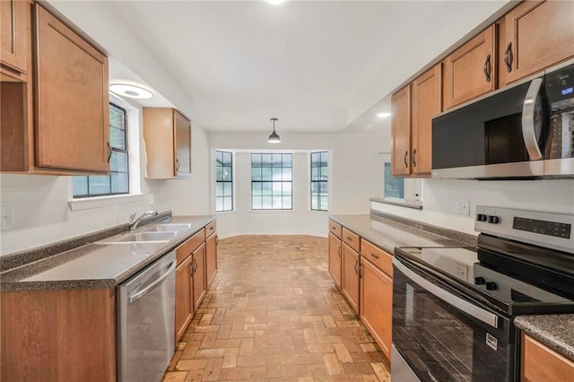 kitchen featuring a sink, dark countertops, brown cabinetry, brick floor, and stainless steel appliances