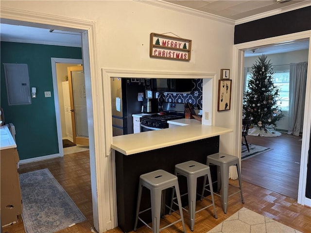 kitchen with parquet floors, stainless steel range, crown molding, electric panel, and a breakfast bar area