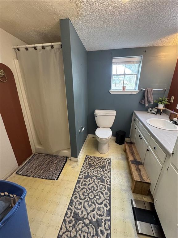 bathroom featuring a textured ceiling, vanity, toilet, and walk in shower