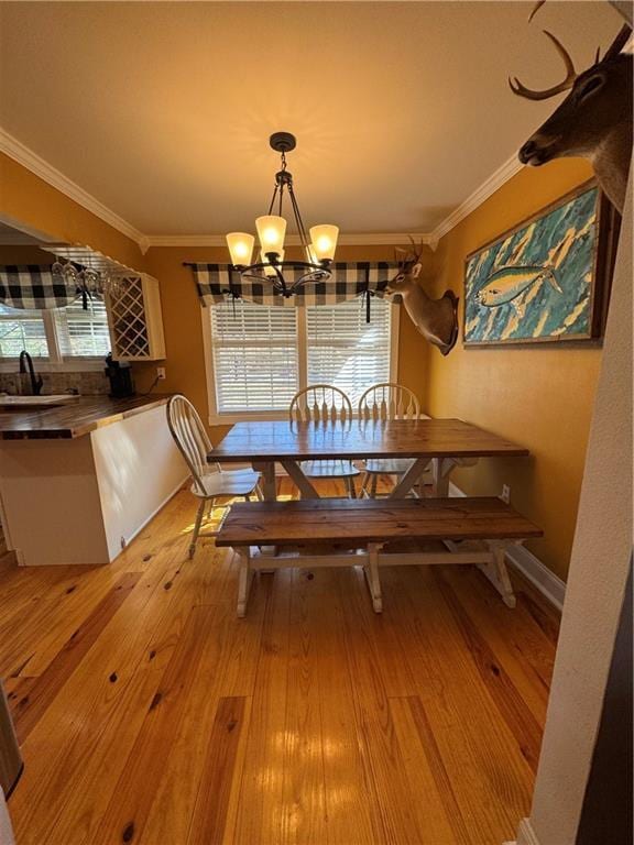 dining room featuring a chandelier, baseboards, crown molding, and light wood finished floors