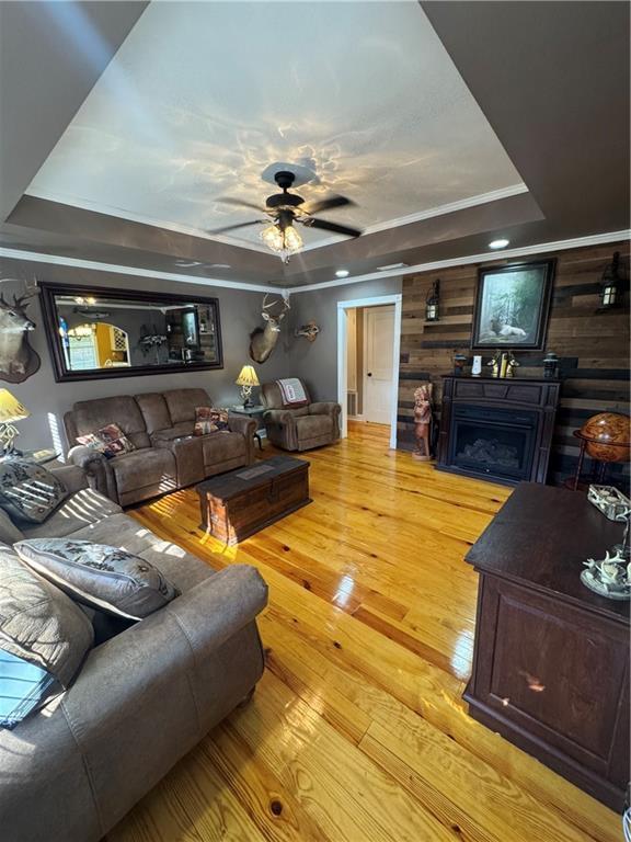 living room with a ceiling fan, a tray ceiling, a fireplace, and light wood finished floors