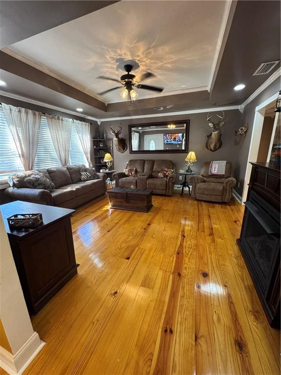 living area with crown molding, a tray ceiling, visible vents, and light wood-style floors