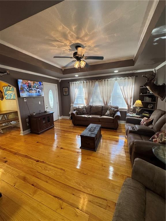 living room with light wood-type flooring, ornamental molding, and a raised ceiling