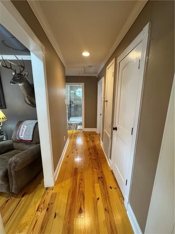 hall featuring baseboards, light wood finished floors, and crown molding