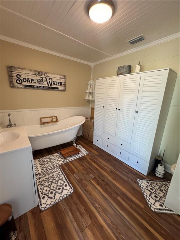 bathroom featuring a soaking tub, visible vents, ornamental molding, wainscoting, and wood finished floors