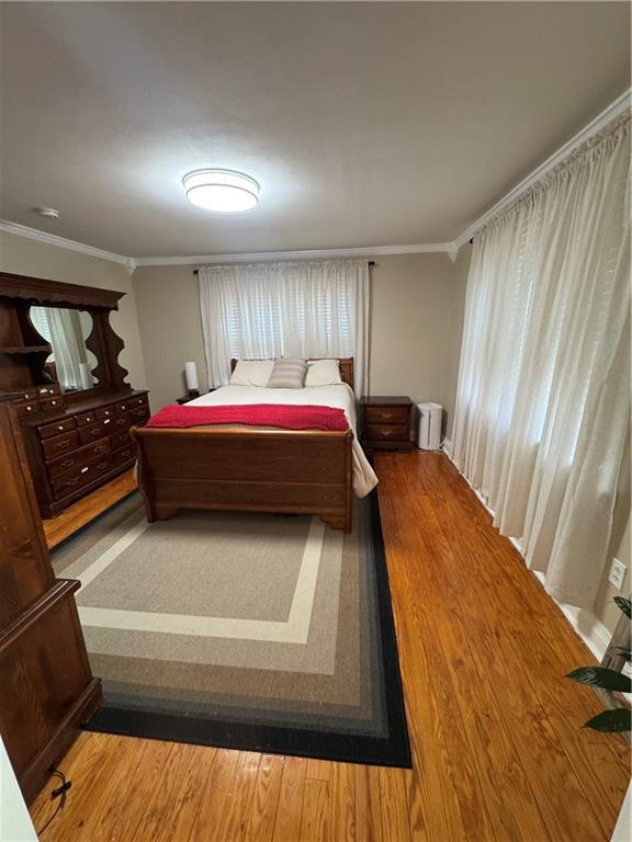 bedroom with ornamental molding and wood finished floors