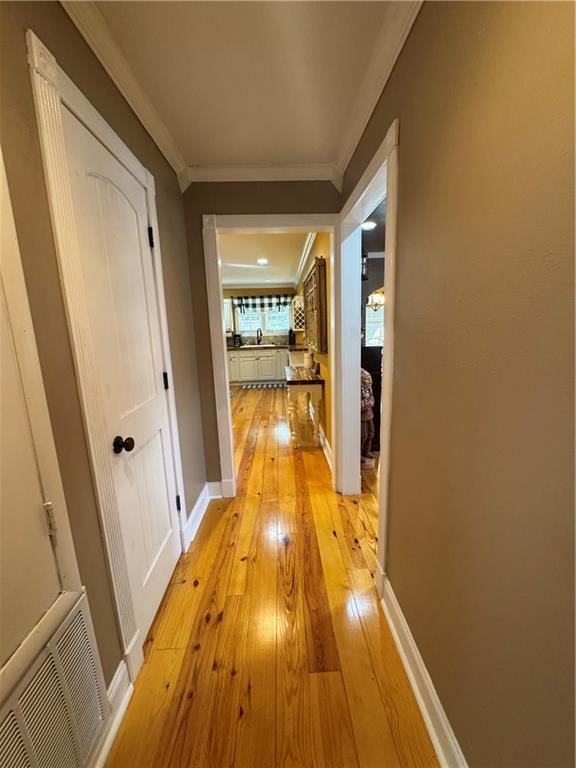 hallway featuring baseboards, light wood-style flooring, visible vents, and crown molding