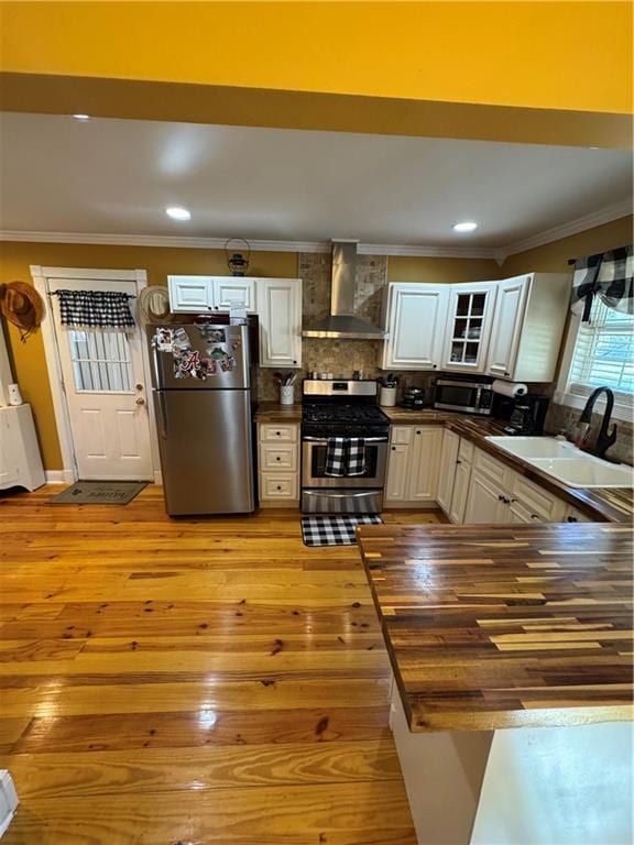 kitchen featuring dark countertops, wall chimney range hood, appliances with stainless steel finishes, and a sink