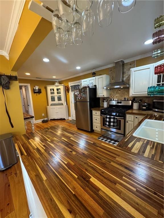 kitchen with a sink, ornamental molding, appliances with stainless steel finishes, dark wood-style floors, and wall chimney exhaust hood