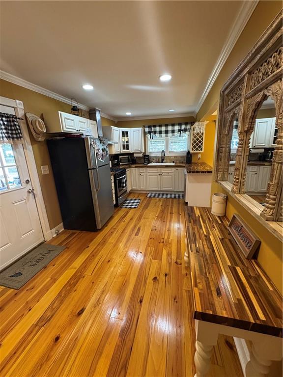 kitchen with stainless steel appliances, a sink, ornamental molding, light wood-type flooring, and a wealth of natural light