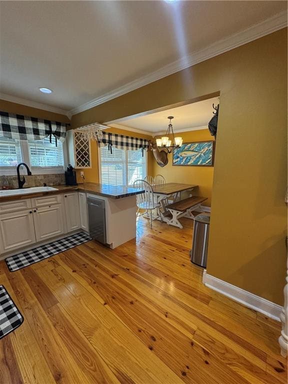 kitchen with light wood-style flooring, a sink, white cabinetry, stainless steel dishwasher, and crown molding