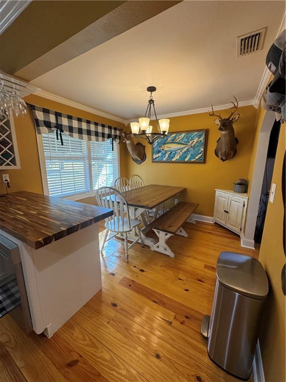 dining space with baseboards, visible vents, crown molding, light wood-type flooring, and a notable chandelier