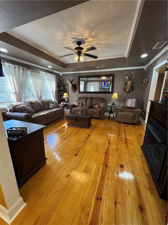 living room with light wood-style floors, a raised ceiling, crown molding, and a ceiling fan