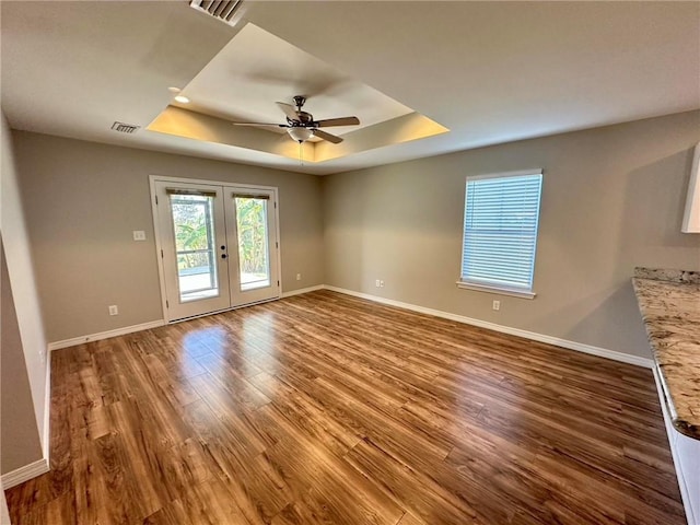 empty room featuring french doors, a raised ceiling, ceiling fan, and wood-type flooring