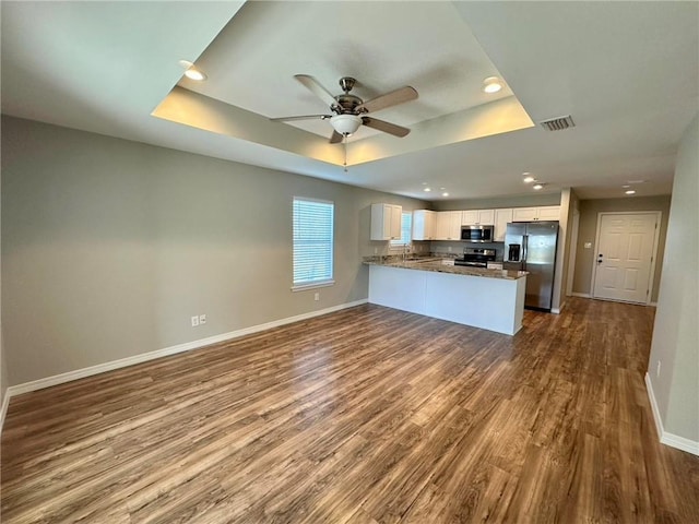 kitchen with white cabinetry, kitchen peninsula, wood-type flooring, a tray ceiling, and appliances with stainless steel finishes