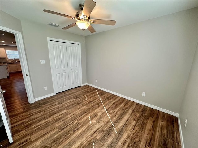 unfurnished bedroom featuring a closet, ceiling fan, dark wood-type flooring, and sink