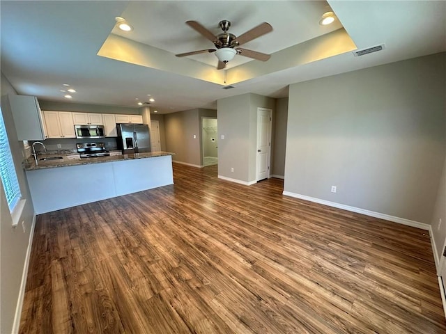 kitchen with kitchen peninsula, light wood-type flooring, stainless steel appliances, and a raised ceiling