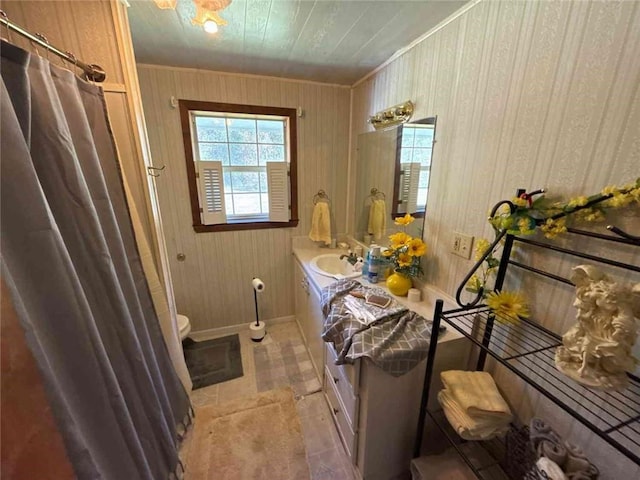 full bath with wooden walls, baseboards, a shower with shower curtain, toilet, and vanity