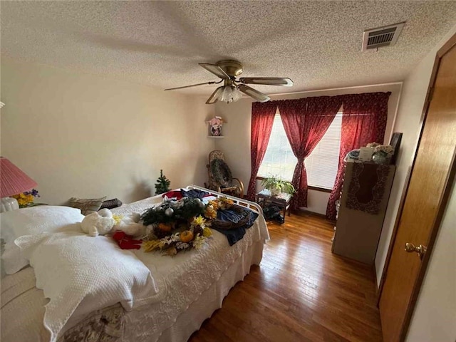 bedroom with a textured ceiling, wood finished floors, visible vents, and a ceiling fan