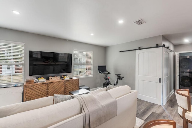 living room featuring light wood-type flooring, plenty of natural light, stacked washer and clothes dryer, and a barn door