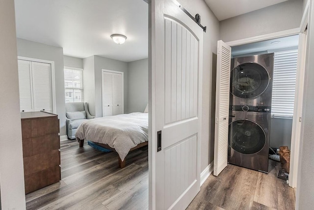 bedroom with stacked washing maching and dryer, a barn door, multiple closets, and hardwood / wood-style flooring